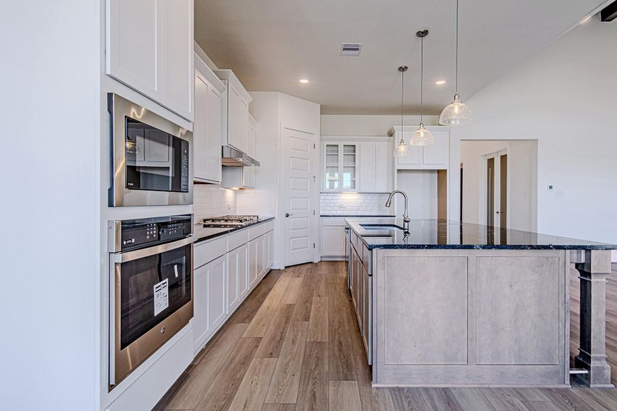 Alternate kitchen view highlighting oven stack, prep space, and cabinetry.