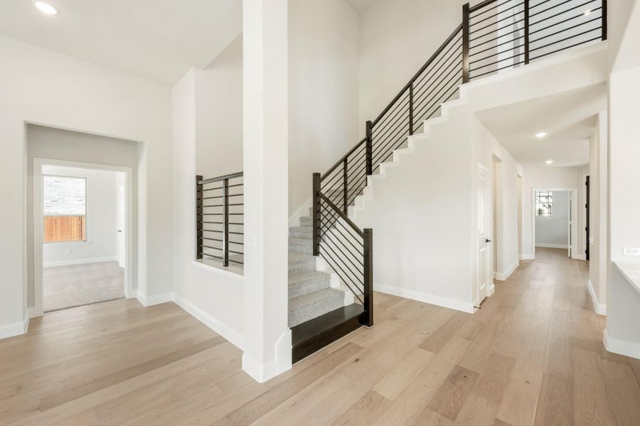 Open foyer with carpeted staircase, black metal railing, and light hardwood floors in a two-story home