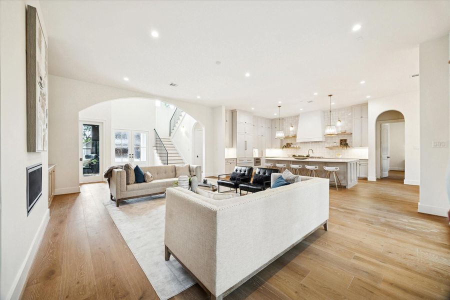 Bright open living space with white oak wood flooring, arched entry to the foyer, and seamless flow into the kitchen.