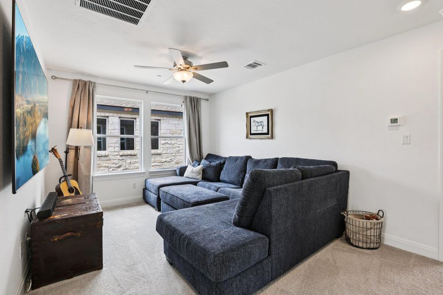 Living area featuring carpeted floors, white walls, and a ceiling fan with integrated lighting