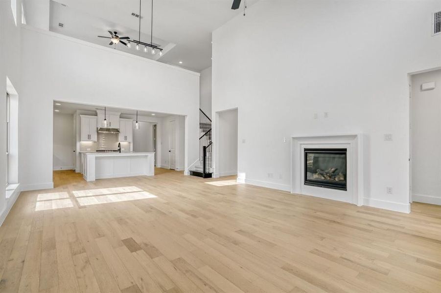 Unfurnished living room with ceiling fan, a glass covered fireplace, light wood-style floors, a high ceiling, and recessed lighting