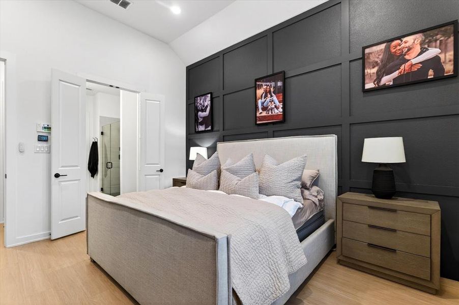 Bedroom featuring a decorative wall, lofted ceiling, and light wood-style floors Bedroom featuring a decorative wall, lofted ceiling, and light wood-style floors