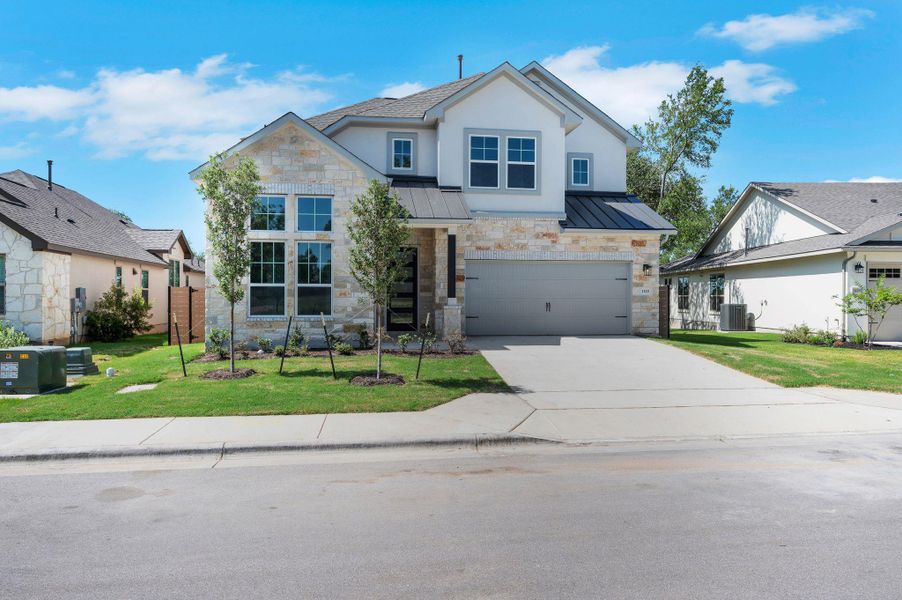 View of front facade with a standing seam roof, a metal roof, an attached garage, and stone siding