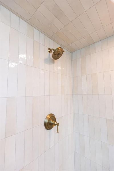 Shower enclosure featuring vertically-stacked rectangular wall tiles, a ceiling with horizontal rectangular tiles, a bronze-finish showerhead, and a matching bronze-finish shower control