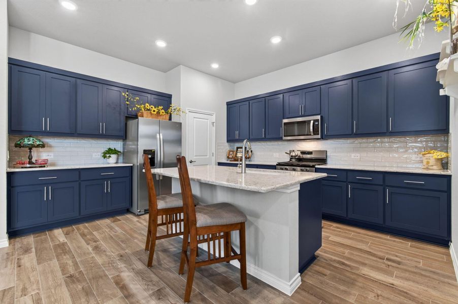 Well-lit kitchen with deep blue cabinetry, sleek stainless steel appliances, and a central island with a breakfast bar. Well-lit kitchen with deep blue cabinetry, sleek stainless steel appliances, and a central island with a breakfast bar.
