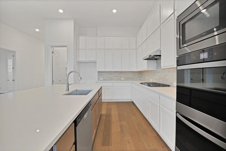 Kitchen featuring tasteful backsplash, a kitchen island with sink, white cabinetry, and appliances with stainless steel finishes