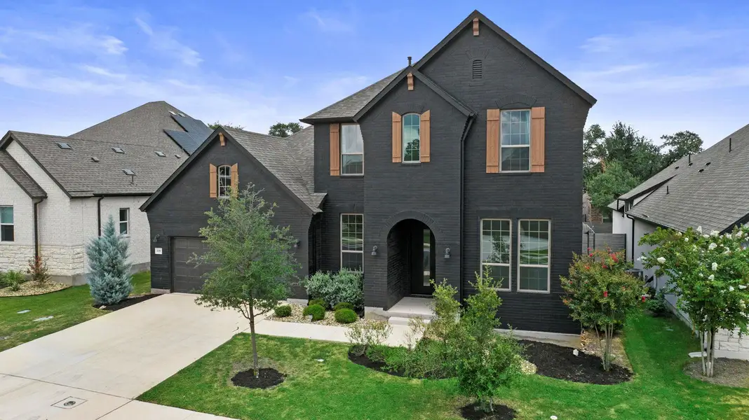 Striking two-story home with modern black exterior, warm wood accents, and lush landscaping, creating an inviting curb appeal.