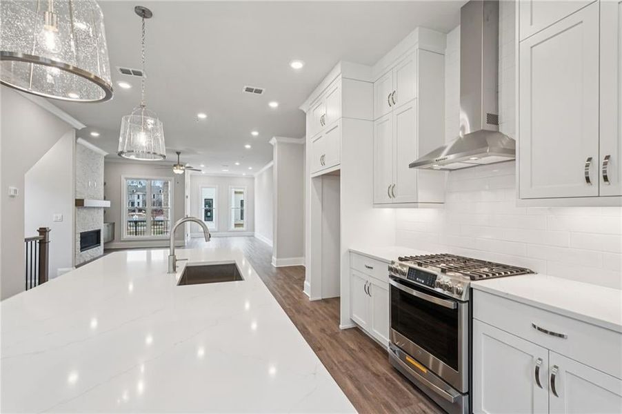 Kitchen with stainless steel range with gas stovetop, dark wood finished floors, white cabinets, ornamental molding, and a fireplace