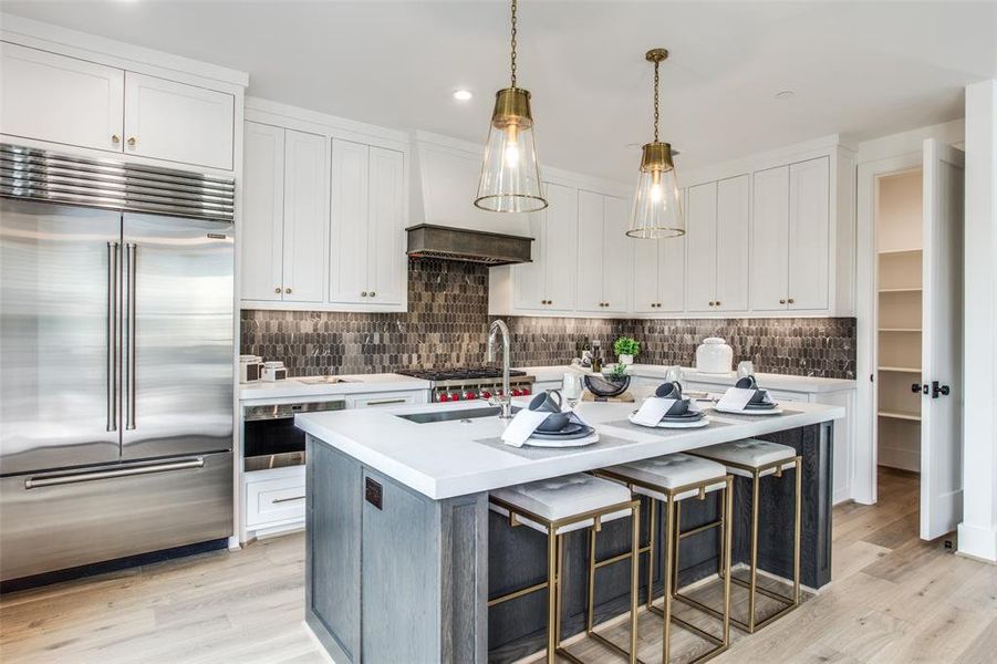 Kitchen with appliances with stainless steel finishes, white cabinetry, light hardwood and an island with sink