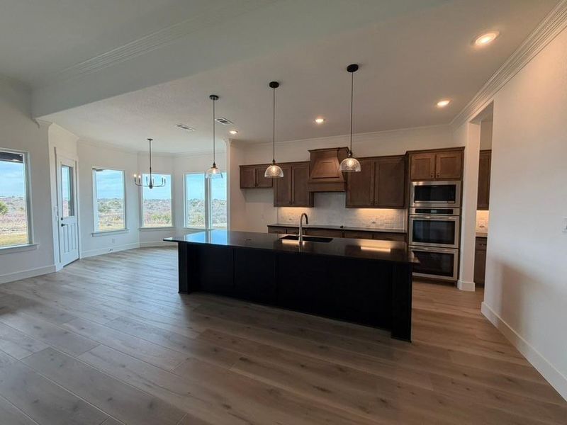 Kitchen featuring ornamental molding, decorative light fixtures, decorative backsplash, an island with sink, and stainless steel appliances