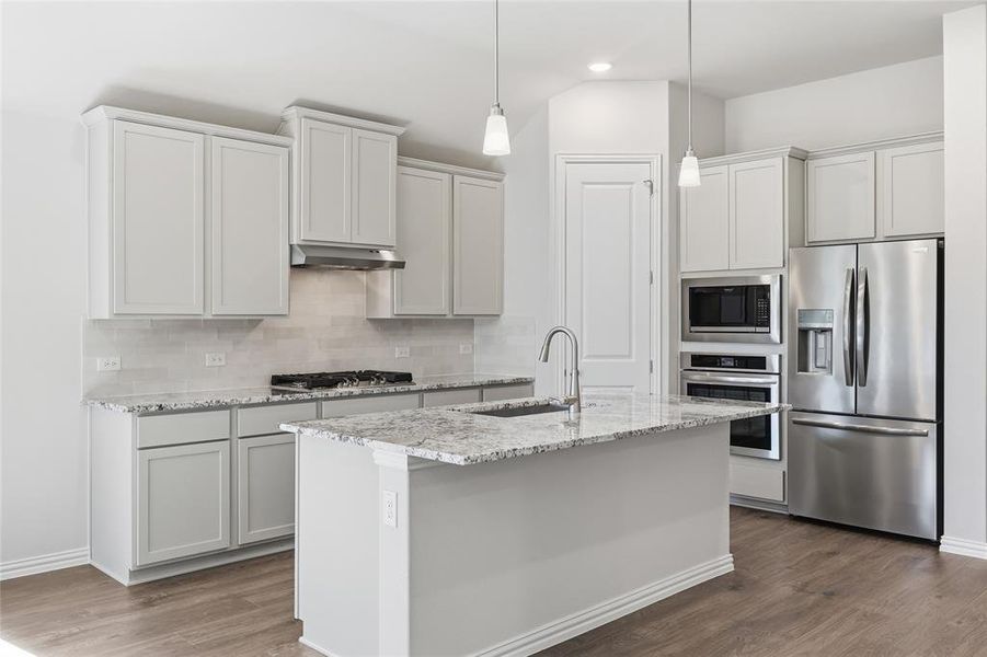 Kitchen featuring stainless steel appliances, light stone countertops, an island with sink, dark wood-style floors, and decorative light fixtures Kitchen featuring stainless steel appliances, light stone countertops, an island with sink, dark wood-style floors, and decorative light fixtures