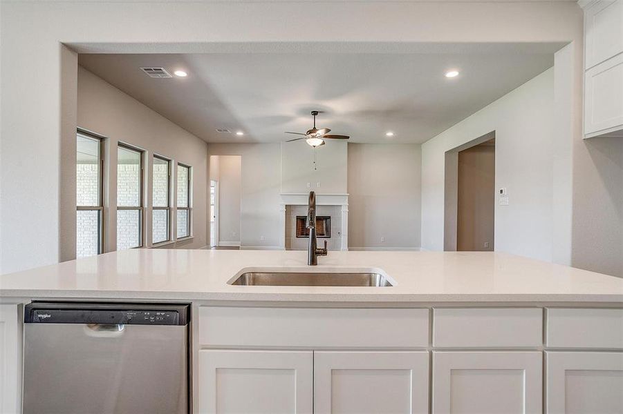 Kitchen with white cabinets, dishwasher, ceiling fan, a fireplace, and sink