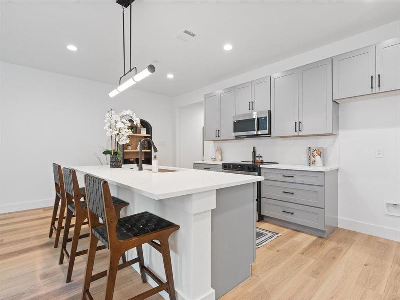 Kitchen with appliances with stainless steel finishes, a sink, visible vents, a breakfast bar area, and gray cabinetry Kitchen with appliances with stainless steel finishes, a sink, visible vents, a breakfast bar area, and gray cabinetry