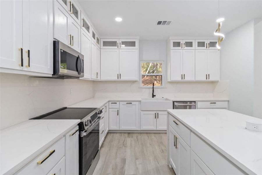 Kitchen with appliances with stainless steel finishes, glass insert cabinets, hanging light fixtures, white cabinetry, and recessed lighting