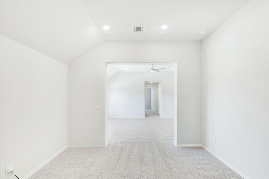 Empty room with white walls, carpet flooring, vaulted ceiling, and open archway leading to adjoining room with ceiling fan.
