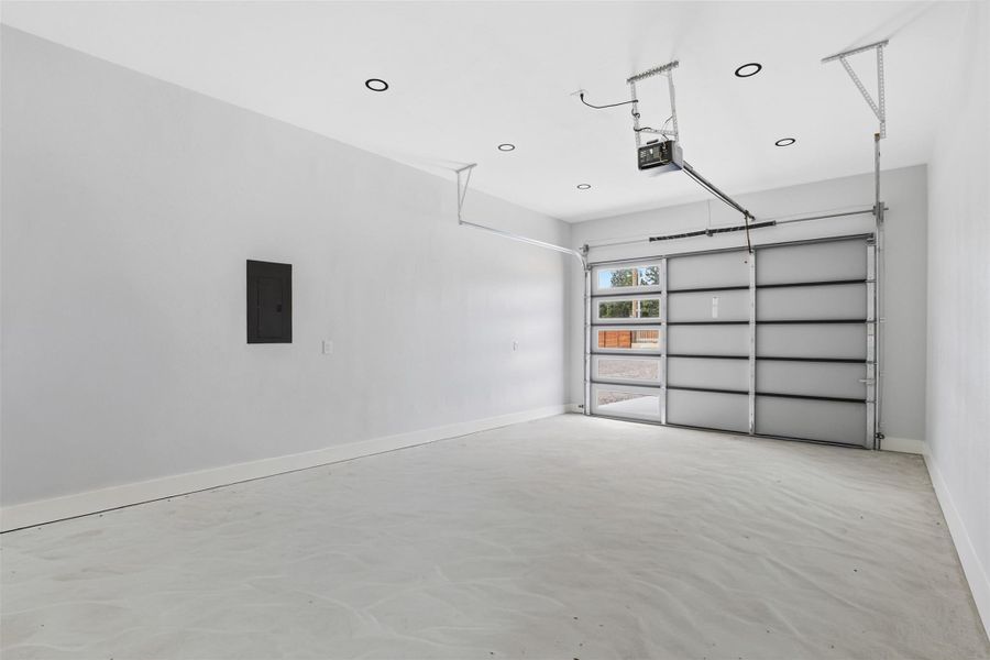 Spacious garage featuring a modern glass panel garage door, recessed ceiling lighting, and a smooth concrete floor