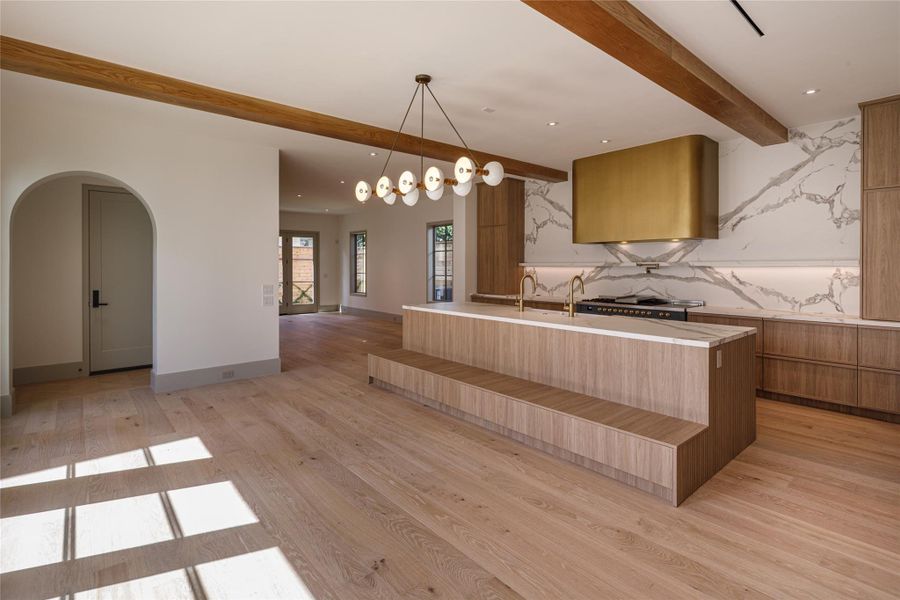 Just finished with warm wood cabinetry, dramatic veined surfaces, exposed wood beams, brass accents, and an oversized island with integrated bench seating. The room was designed to be used, not simply admired.