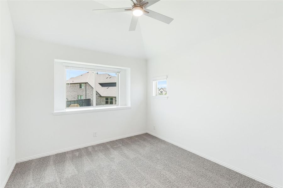 Empty bedroom with vaulted ceiling, ceiling fan, gray carpet, and two windows overlooking neighboring homes Empty bedroom with vaulted ceiling, ceiling fan, gray carpet, and two windows overlooking neighboring homes