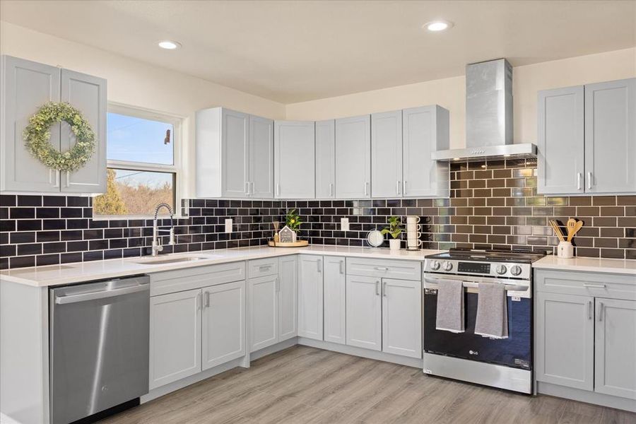 Kitchen with wall chimney exhaust hood, sink, light wood-type flooring, stainless steel appliances, and backsplash