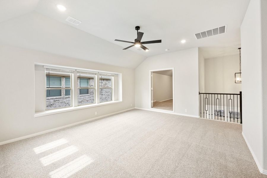 Spacious empty room with vaulted ceiling, ceiling fan, carpet flooring, and open staircase railing nearby Spacious empty room with vaulted ceiling, ceiling fan, carpet flooring, and open staircase railing nearby
