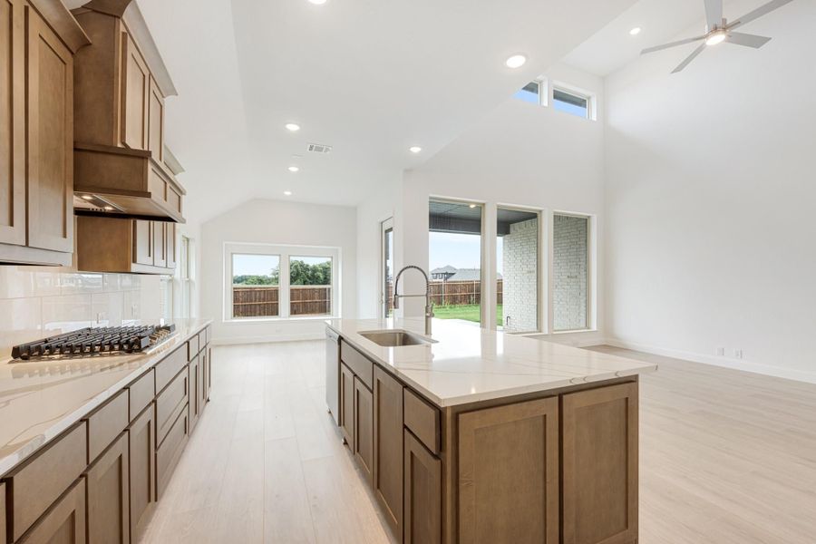 Open kitchen with wood cabinets, large island, quartz countertops, and vaulted ceiling open to living area Open kitchen with wood cabinets, large island, quartz countertops, and vaulted ceiling open to living area