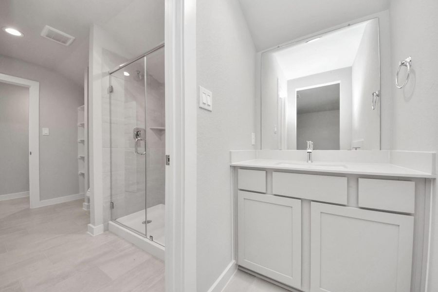 Experience convenience in the secondary bathroom, designed for Jack and Jill arrangements, now with a separate vanity area. This well-appointed space showcases stylish tile flooring, a bath/shower combo with an elegant tile surround, and light-stained wood cabinets. The beautiful light countertop adds a touch of sophistication, combining functionality and aesthetics seamlessly. Sample photo of completed home with similar floor plan. Actual colors and selections may vary.