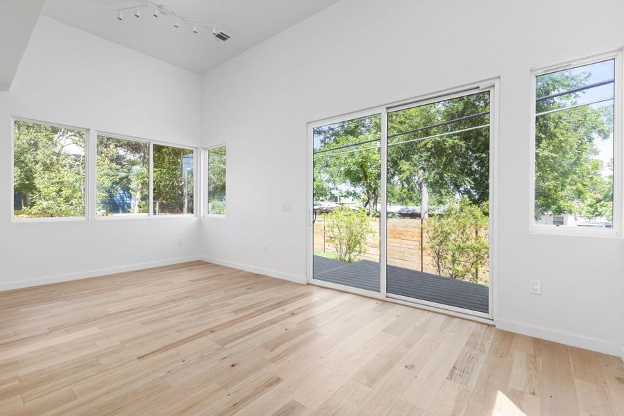 Unfurnished room featuring healthy amount of natural light, light wood-style floors, rail lighting, and baseboards