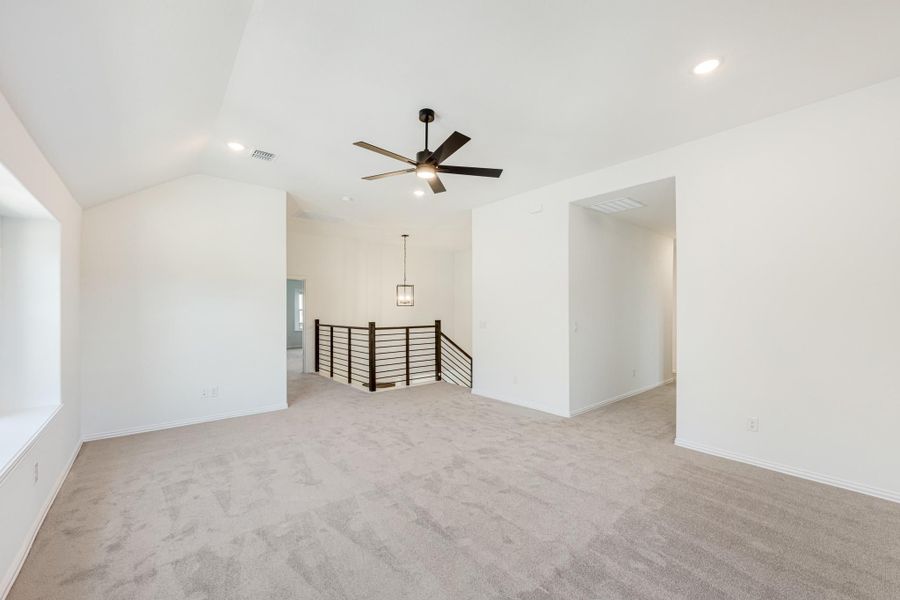 Open upstairs living area with vaulted ceiling, ceiling fan, carpet, and metal stair railing Open upstairs living area with vaulted ceiling, ceiling fan, carpet, and metal stair railing