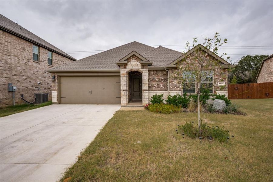 French country inspired facade featuring roof with shingles, brick siding, concrete driveway, a garage, and stone siding