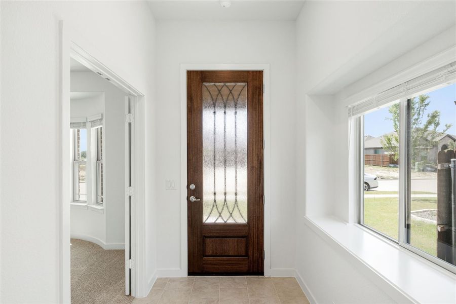 Bright entryway with dark wood front door featuring decorative glass panel and white walls