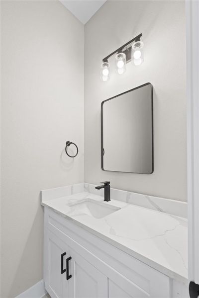 Half bathroom features a modern design with a sleek white vanity, black fixtures, and a marble countertop. The space is well-lit with a three-bulb light fixture above a rectangular mirror, creating a clean and sophisticated look.