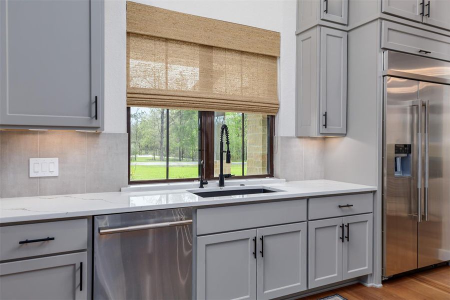 The matte black hardware pulls are complimented by the more delicate champagne brass hardware.  The deep back sink with motion operated faucet, custom cabinets, counter depth refrigerator and tranquil views surely make light of any kitchen chores.  The ceramic block tile backsplash also ties in design connection with the feature fireplace.