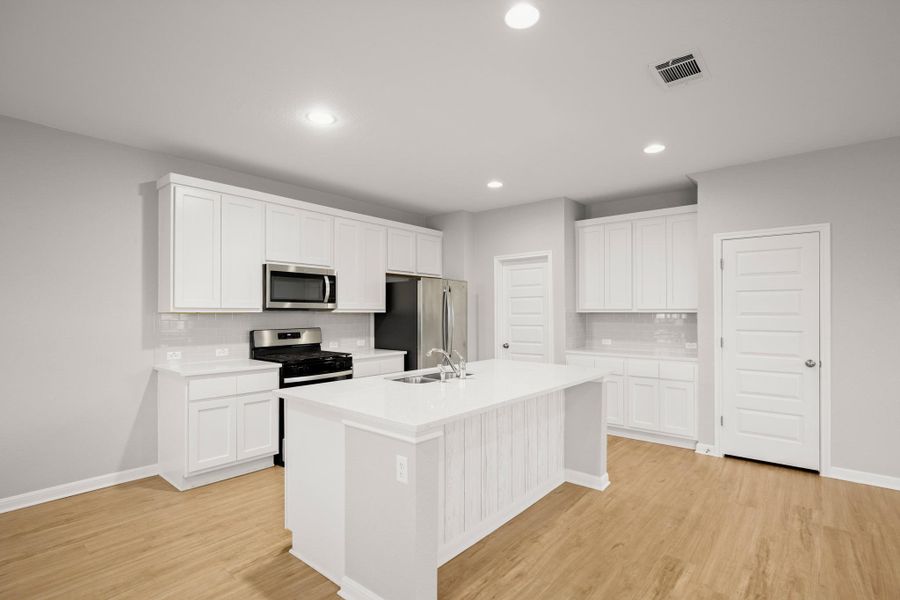 Kitchen with appliances with stainless steel finishes, decorative backsplash, light wood-style floors, a kitchen island with sink, and recessed lighting