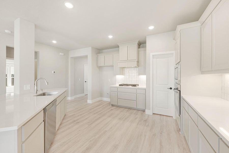 Open kitchen with light gray cabinets, white countertops, tile backsplash, and light wood floors