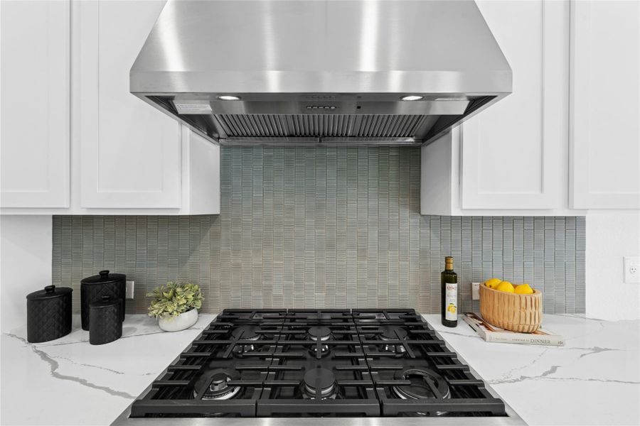 Kitchen featuring range hood, quartz countertops, 6 burner gas stovetop, and custom backsplash Kitchen featuring range hood, quartz countertops, 6 burner gas stovetop, and custom backsplash