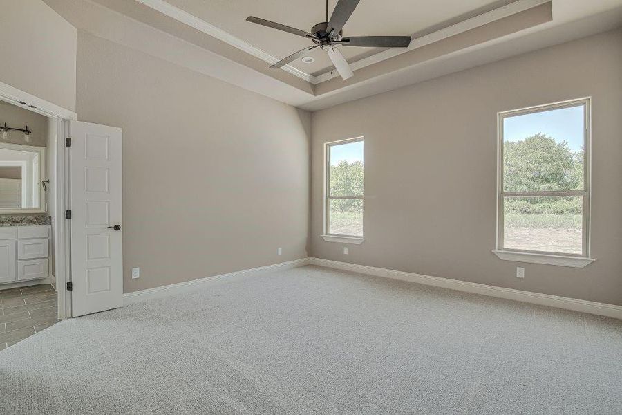 Unfurnished bedroom featuring multiple windows, connected bathroom, light tile patterned floors, and ceiling fan