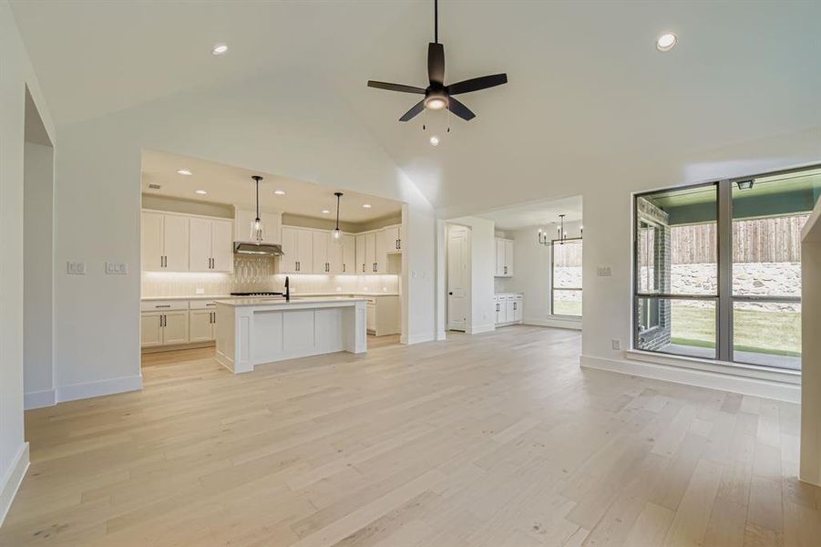 Unfurnished living room with ceiling fan, light wood finished floors, a chandelier, and a high ceiling
