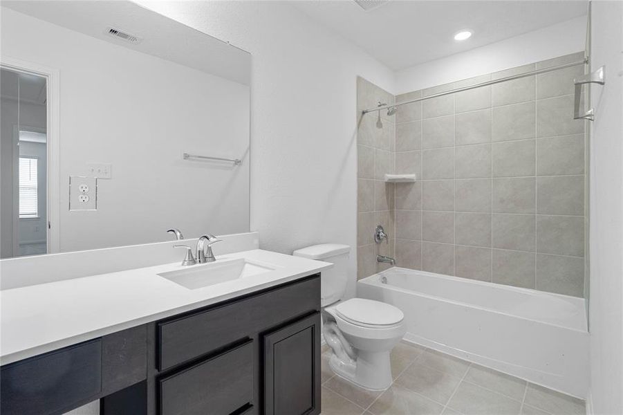 Secondary bath features tile flooring, bath/shower combo with tile surround, stained wood cabinets, beautiful light countertops, mirror, sleek fixtures and modern finishes.