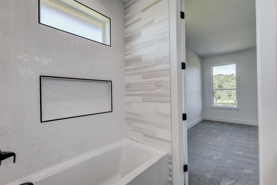 White soaking tub with textured white tile surround, black-framed shower niche, and rectangular transom window White soaking tub with textured white tile surround, black-framed shower niche, and rectangular transom window