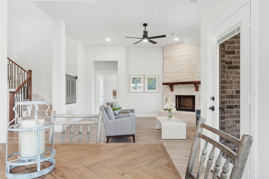 Open living room with stone fireplace, ceiling fan, gray seating, and herringbone wood floors near staircase Open living room with stone fireplace, ceiling fan, gray seating, and herringbone wood floors near staircase