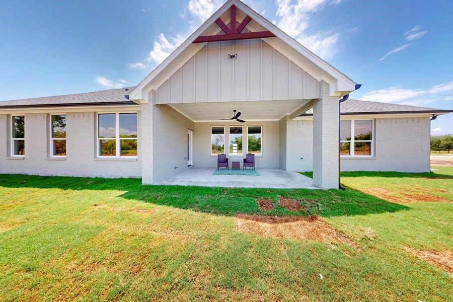 Back of house featuring a ceiling fan, brick siding, a patio area, board and batten siding, and a yard