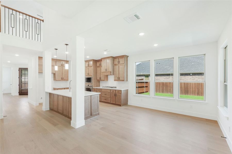 Open-concept kitchen and living area with wood cabinets, kitchen island, and light hardwood floors under high ceilings. Open-concept kitchen and living area with wood cabinets, kitchen island, and light hardwood floors under high ceilings.