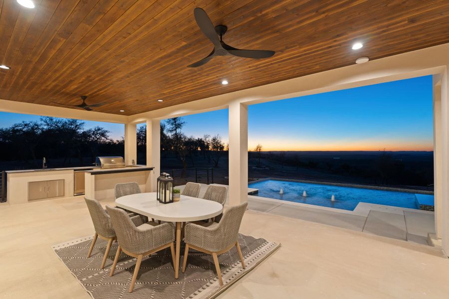 Outdoor living with ample covered area and outdoor kitchen with grill, sink, mini refrigerator and bar area.