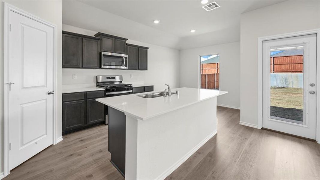 Kitchen featuring stainless steel appliances, a center island with sink, recessed lighting, light stone counters, and light wood finished floors