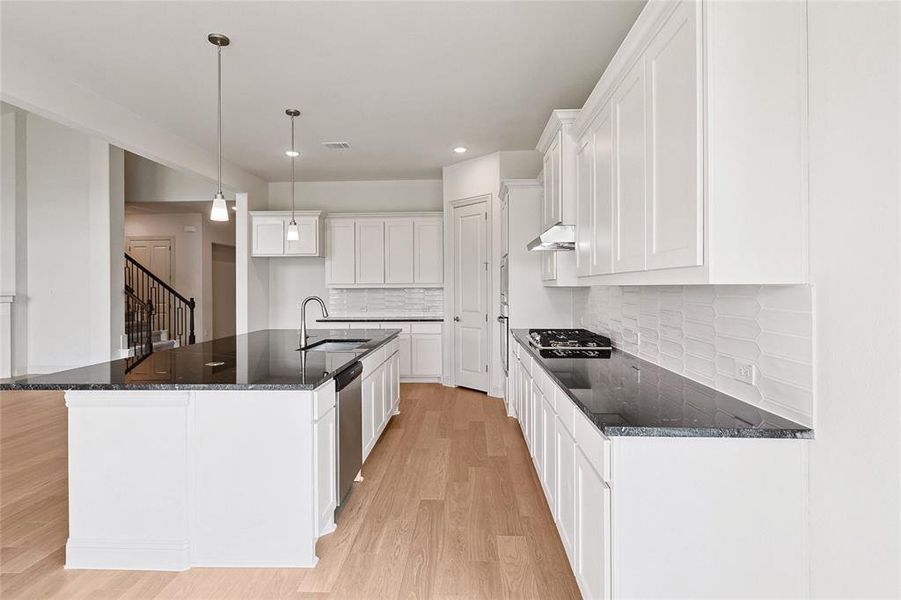 Kitchen featuring white cabinetry, backsplash, a center island with sink, and light hardwood / wood-style flooring