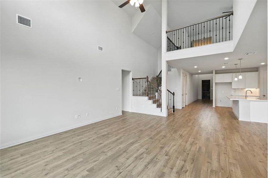 Unfurnished living room with light wood finished floors, a towering ceiling, a ceiling fan, stairs, and recessed lighting