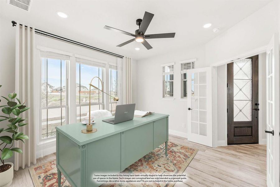 Home office with light wood floors, ceiling fan, large windows, and green desk near front entry door Home office with light wood floors, ceiling fan, large windows, and green desk near front entry door