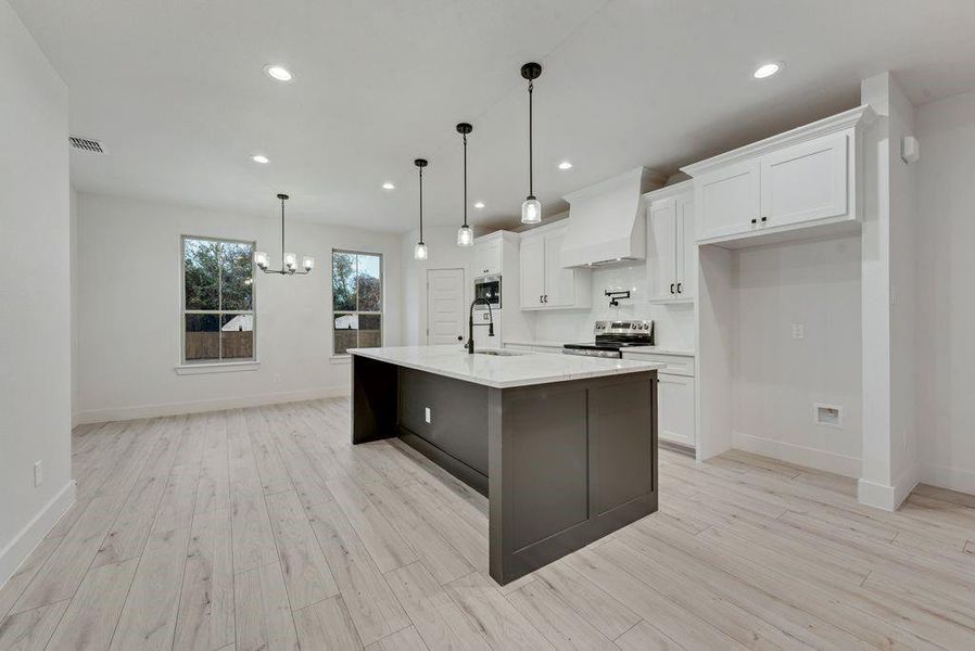 Kitchen with white cabinets, recessed lighting, hanging light fixtures, custom exhaust hood, and a center island with sink