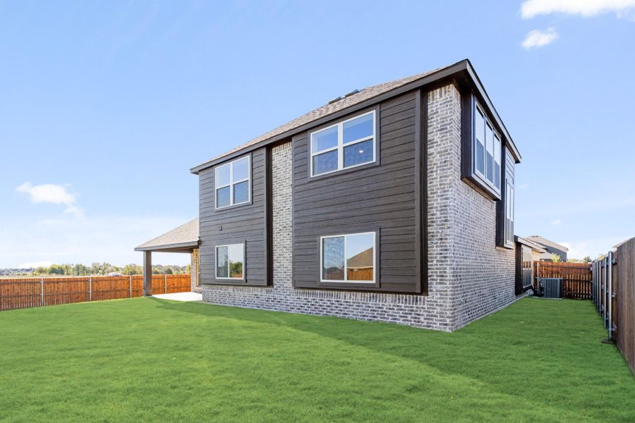 Two-story home rear exterior with dark siding, brick accents, covered patio, and fenced backyard with green lawn