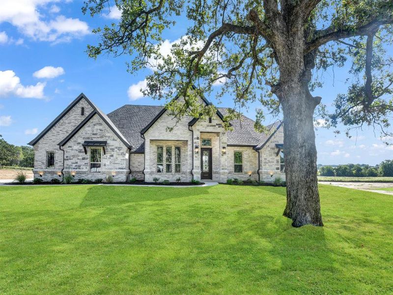 French country inspired facade with a front yard and stone siding